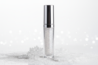 Create a picture of a glass lip gloss with a silver metalic top filled with clear white sparkly lip gloss inside with snow flakes or white glitter sitting around the container of lip gloss 
